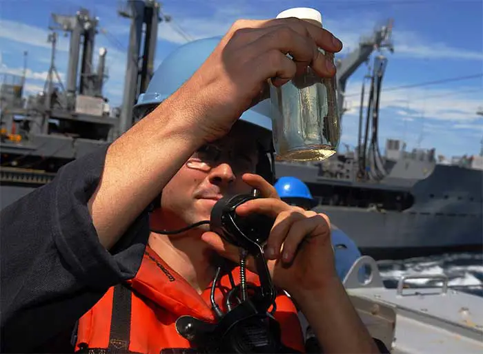 یک دریانورد نمونهای از سوخت جت JP-5 را روی یک ناو حمل و نقل آبی-خاکی بررسی میکند